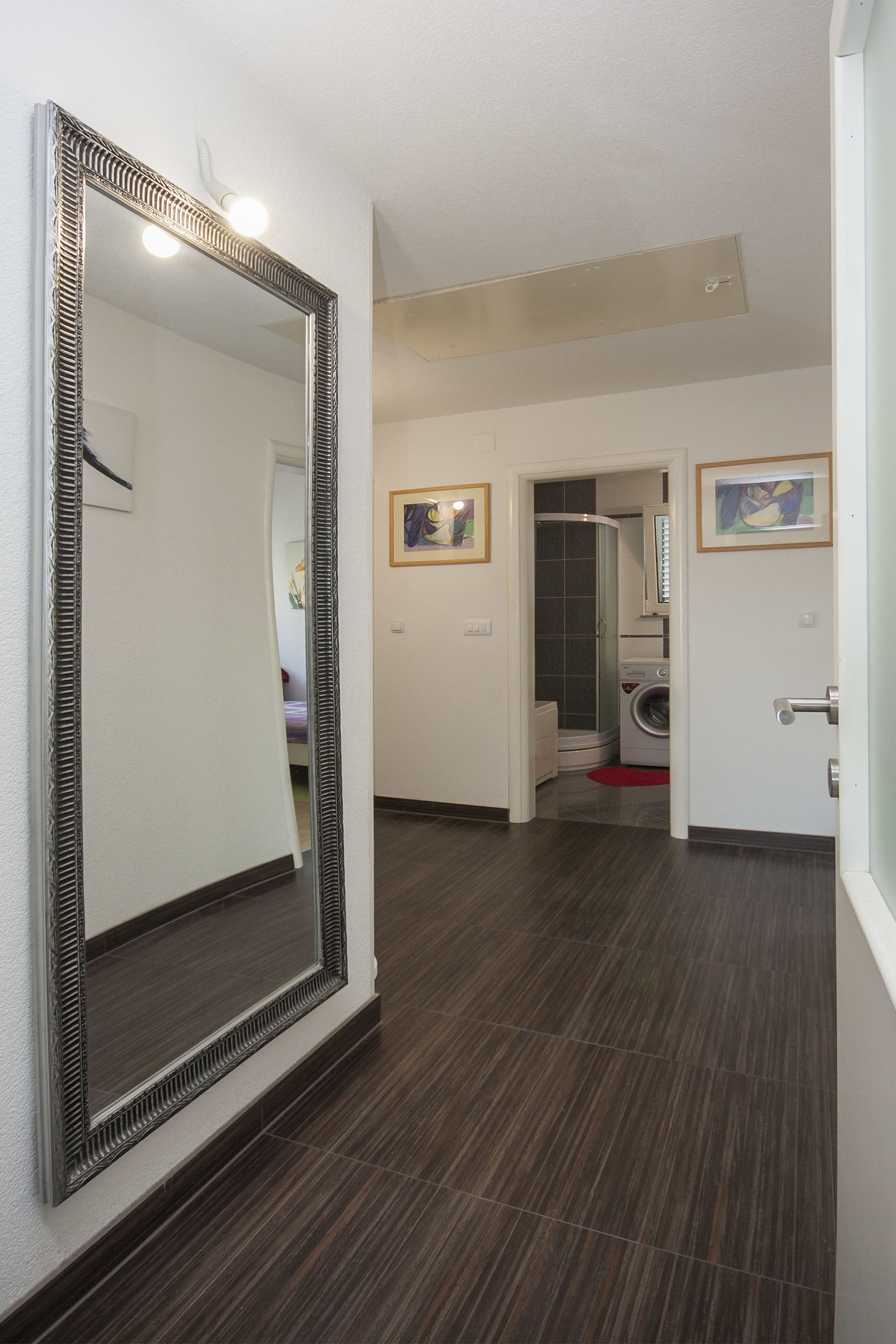 A hallway with a large mirror, a washing machine, and a shower area.