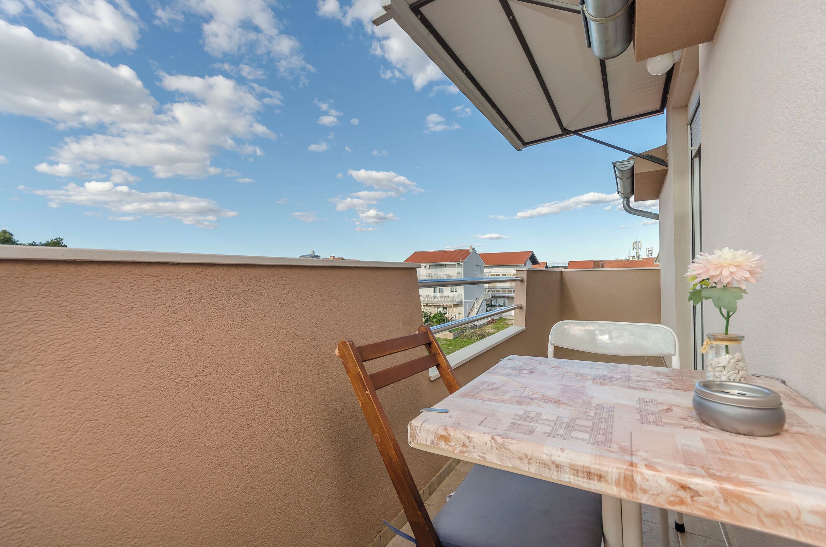 A balcony with a table and chair, a potted plant, and a view of buildings in the background.