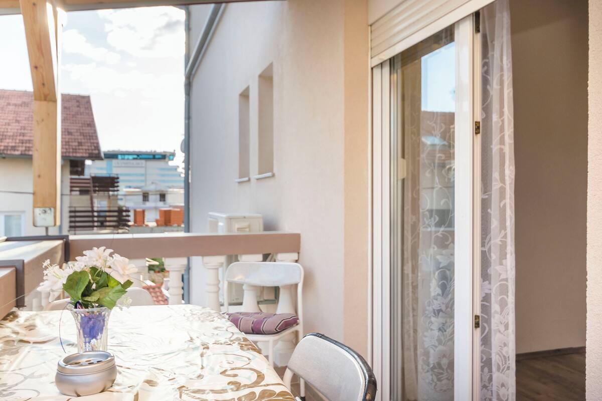 A balcony with a table set for two, a chair, and a vase with flowers.