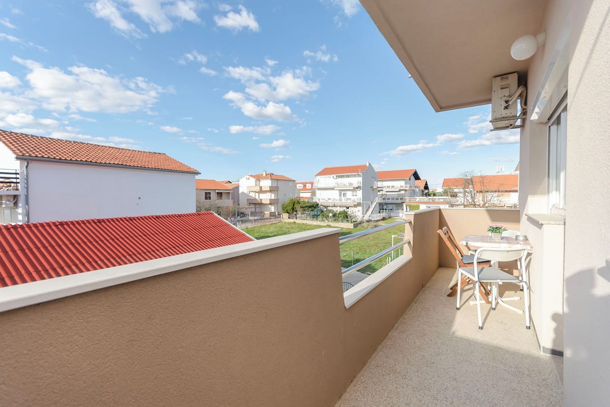 A balcony with a red-tiled roof, a small table with chairs, and a view of neighboring buildings.