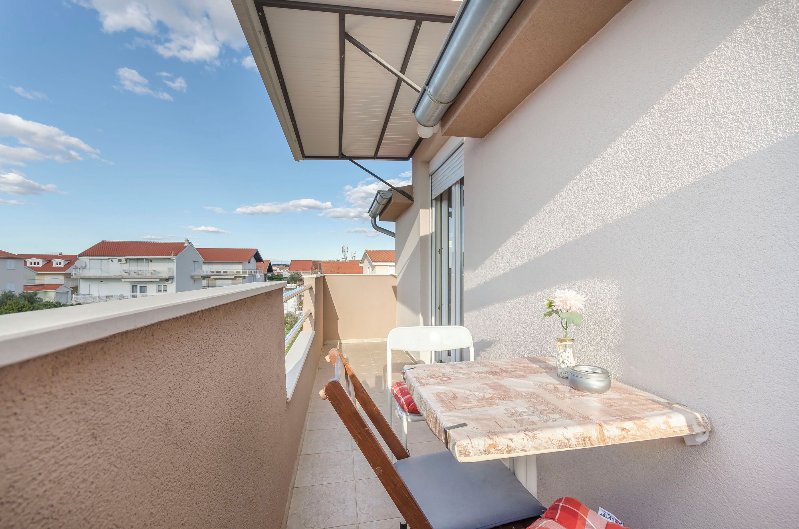 A balcony with a table, chairs, and a vase with flowers.