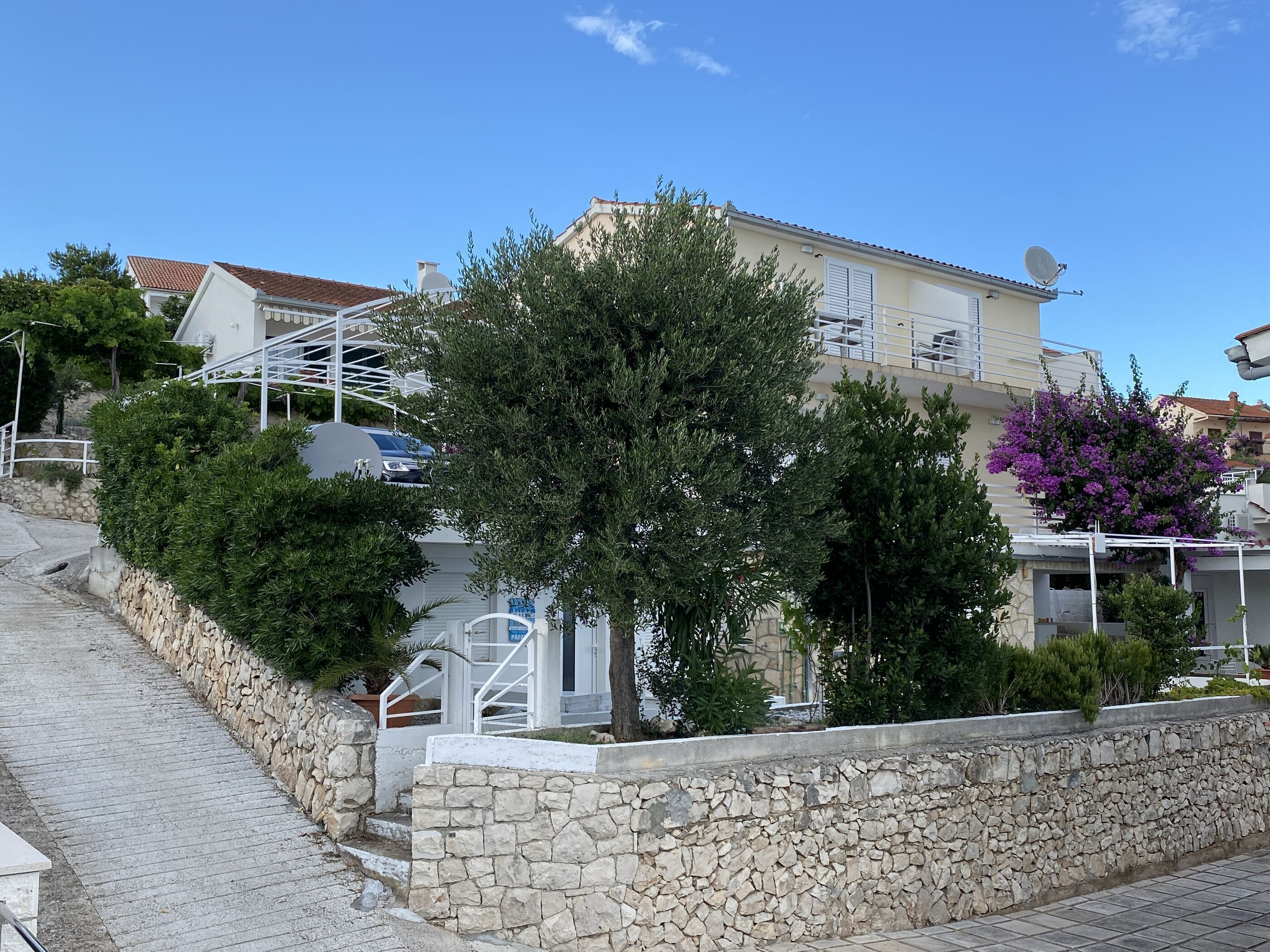 A residential building with a stone retaining wall, a staircase, and a satellite dish.