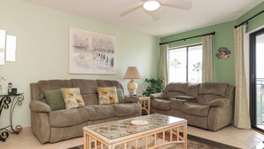 Ein Wohnzimmer mit zwei beigefarbenen Sofas, einem Glastisch, einer Lampe und einem Gemälde an der Wand.