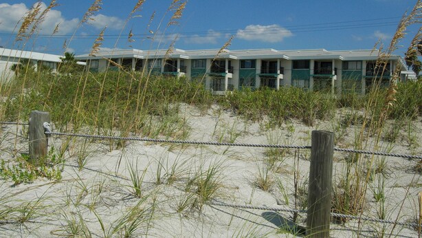 Ein Küstenmotel mit mehreren Zimmern, einem Sandstrand davor und einem strahlend blauen Himmel.