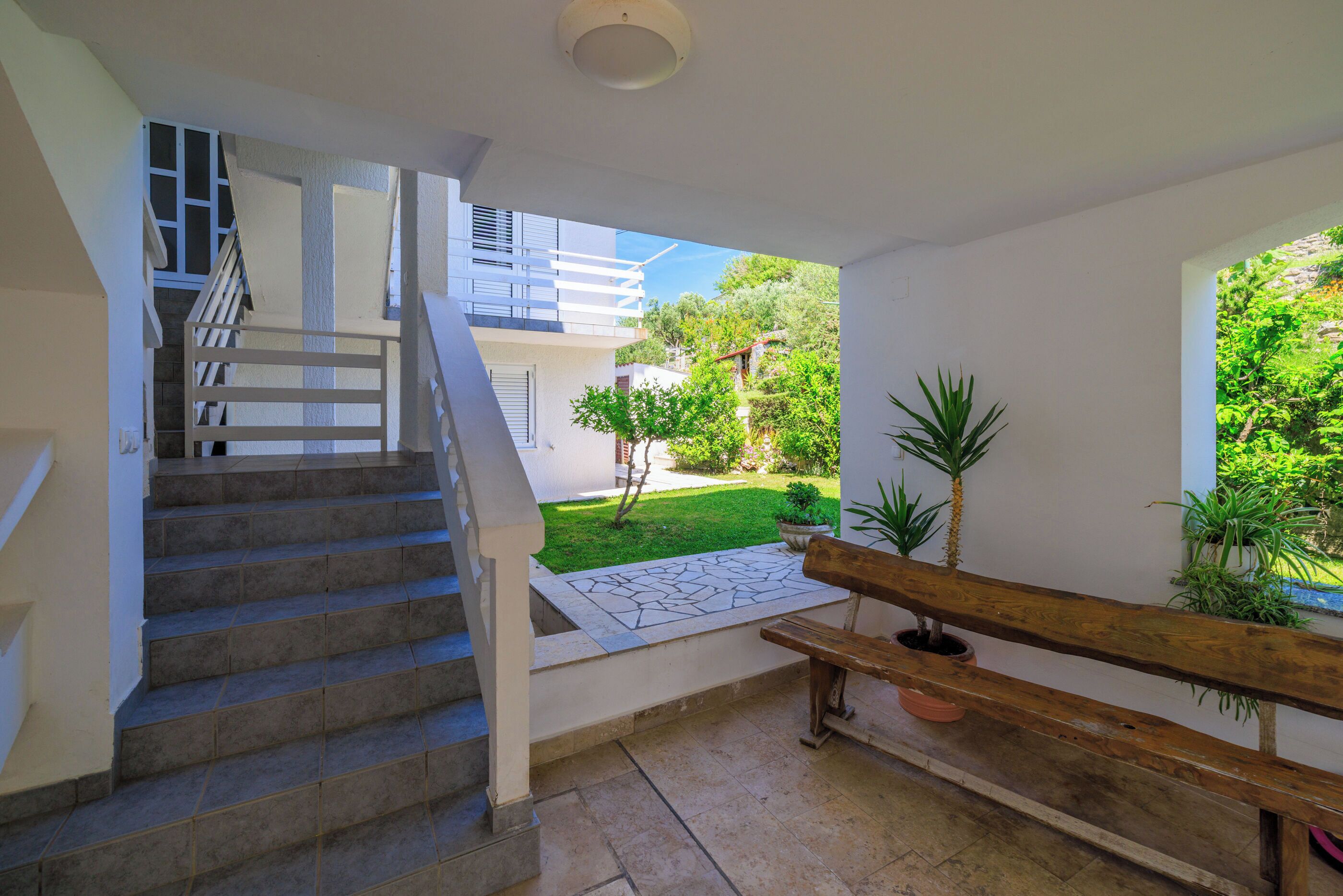 A staircase leading to a balcony with a view of a garden and a building.