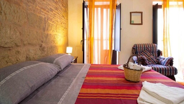 A room with a bed, a chair, a basket, and a window with curtains. - Panorama Studio 'Casa a Chiazzetta' (Castelbuono)
