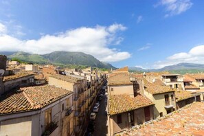 A street view of a town with terracotta-tiled buildings, a clear sky, and mountains in the background.