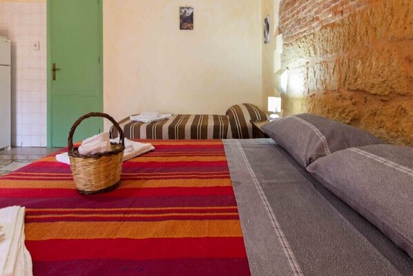 A room with a bed, a sofa, a wicker basket with towels, a green door, and a stone wall.