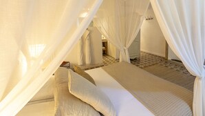 A bedroom with a bed covered by white curtains, a bedside table, and a patterned rug. - Chambre Béguin ou Mantille (30M2) - 3 people (Avignon)