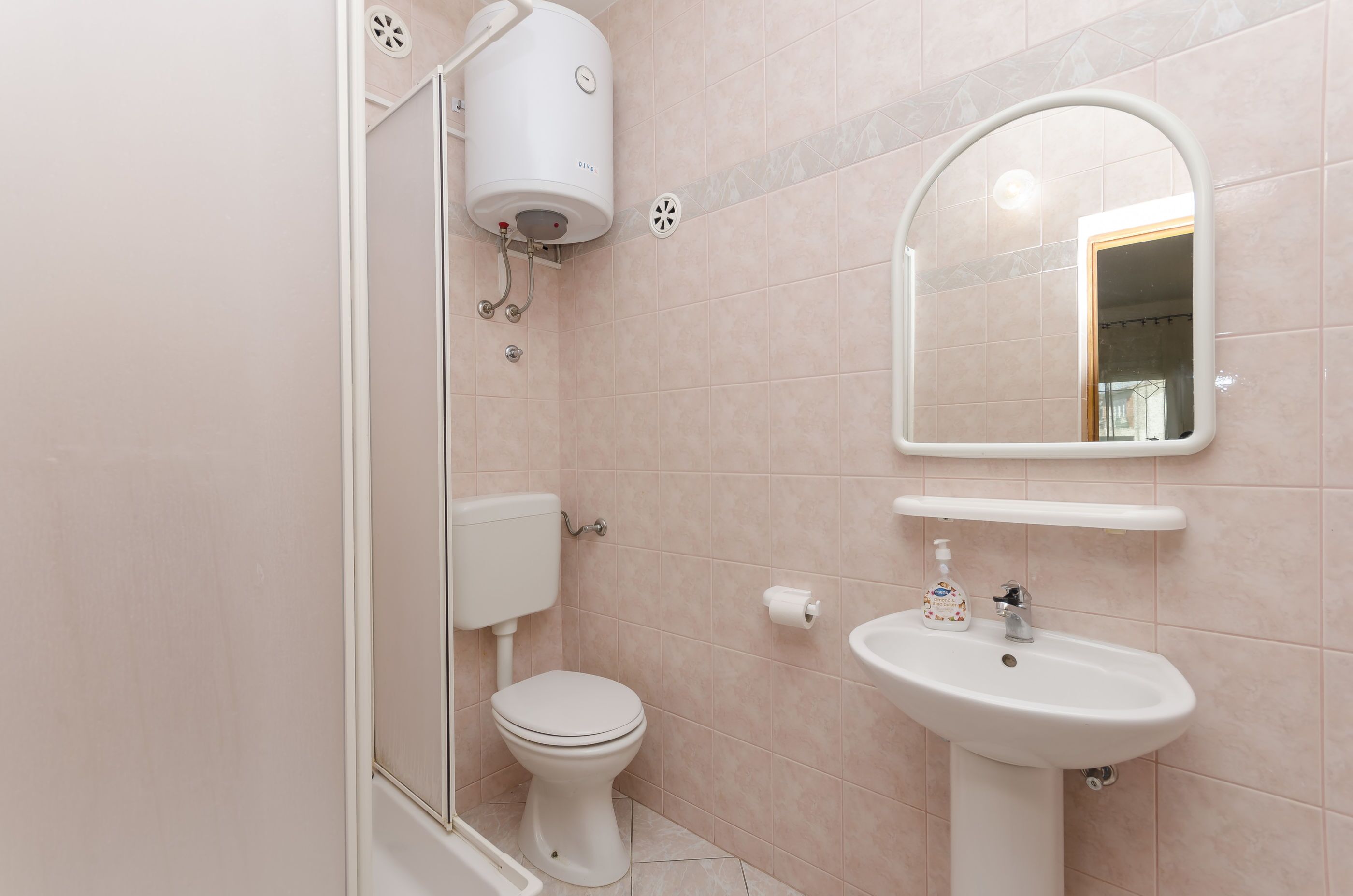 A bathroom with a toilet, sink, mirror, and shower.