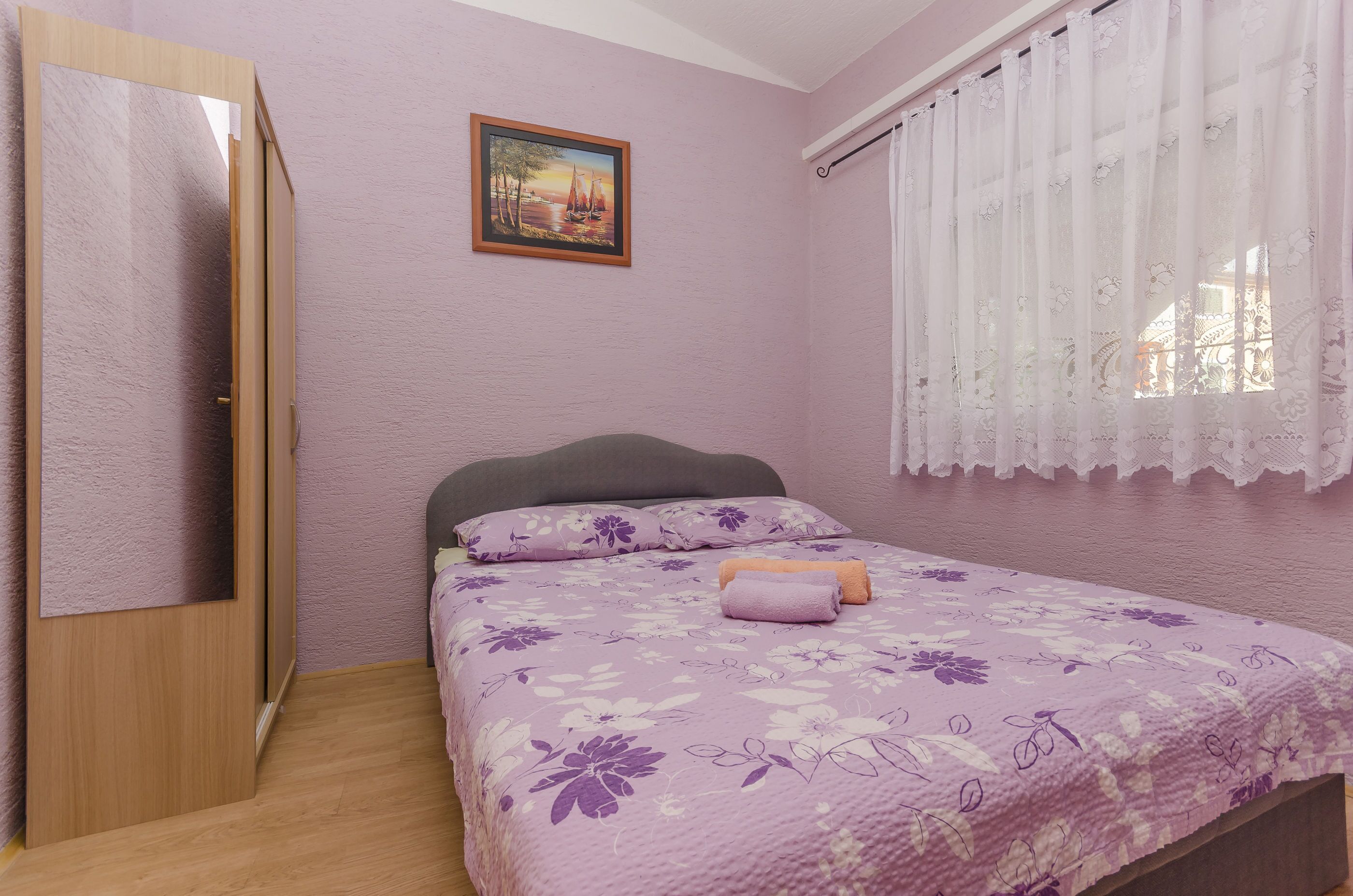 Une chambre à coucher avec un lit, une armoire, un tableau au mur et une fenêtre avec des rideaux.