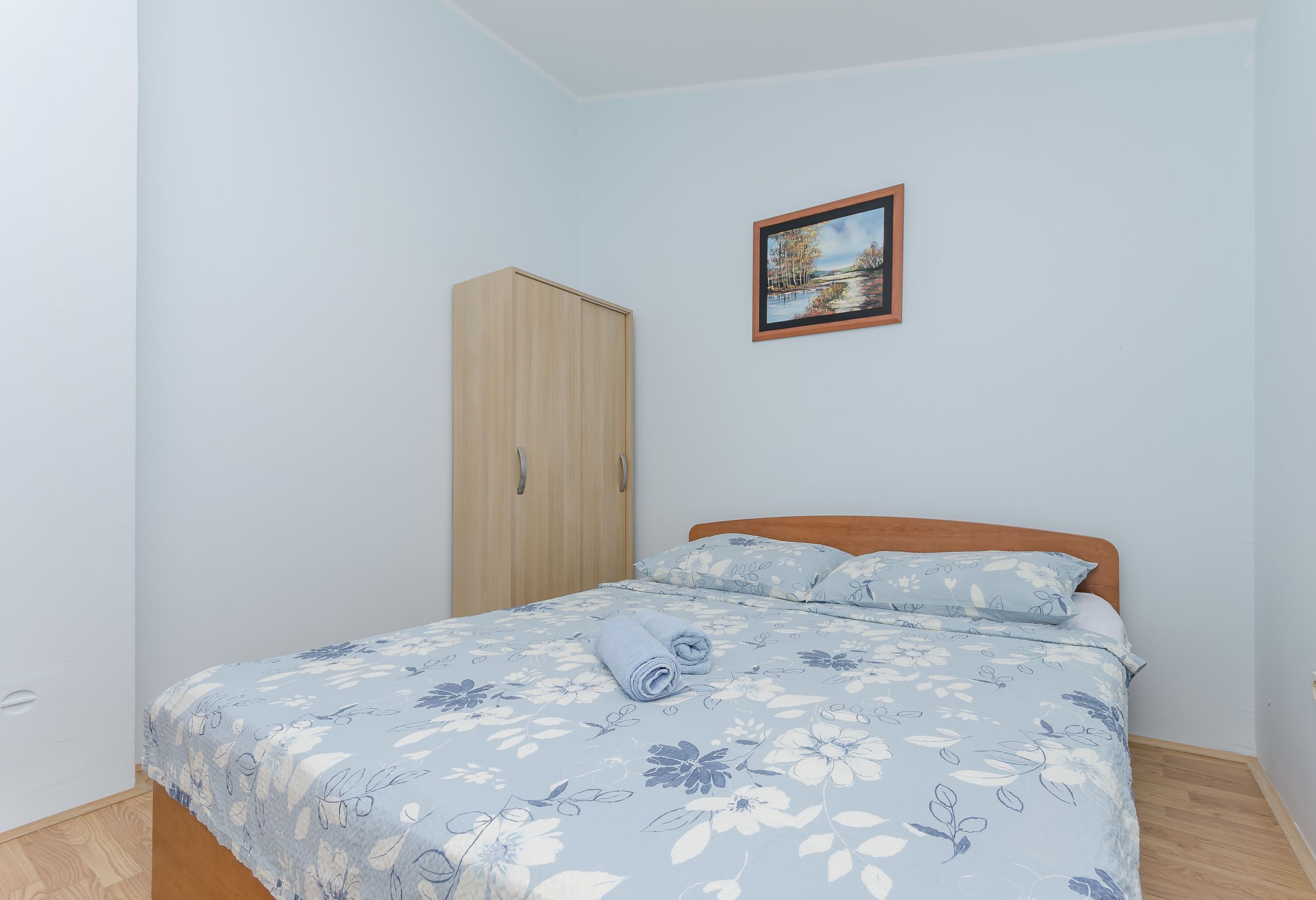 A bedroom with a bed, a wooden wardrobe, and a framed picture on the wall.