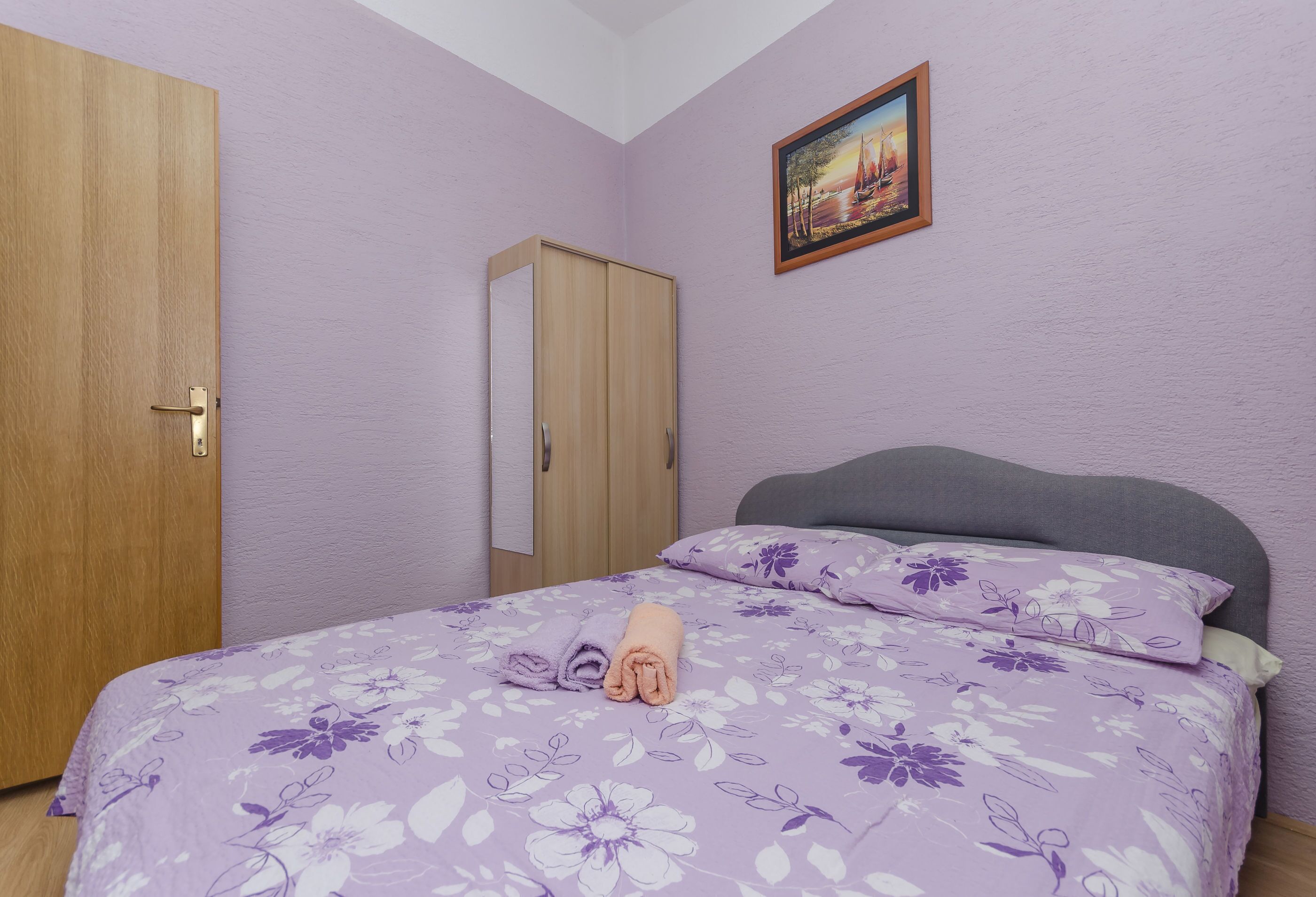 A bedroom with a bed, a wooden wardrobe, and a painting on the wall.