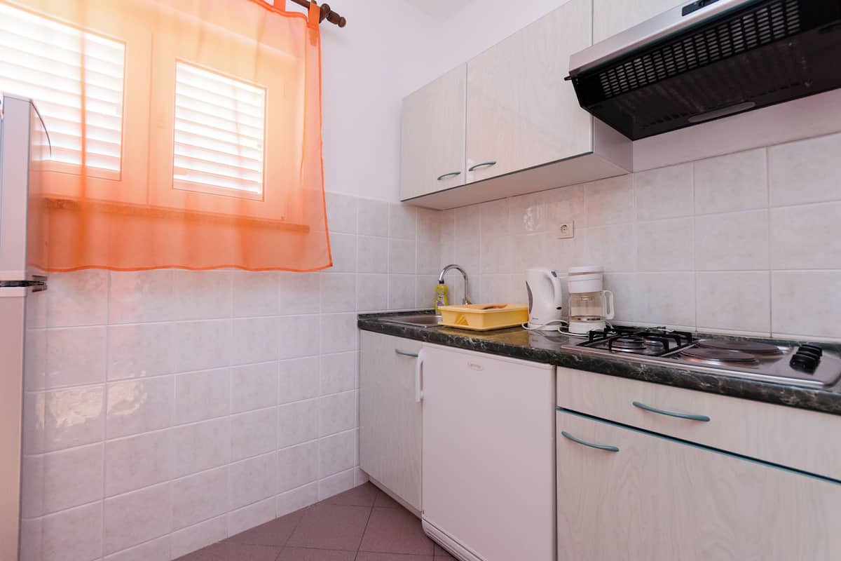 Une cuisine de taille réduite, avec des meubles blancs, une cuisinière à gaz, une machine à café et un réfrigérateur.