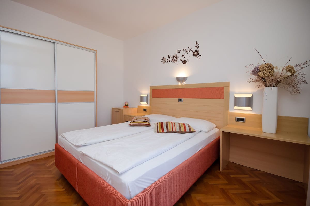 Un dormitorio ordenado con cama, mesitas de noche, armario e iluminación fijada a la pared.