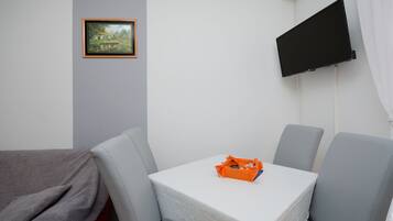 A hotel room with a bed, a small table with an orange basket, and a TV mounted on the wall.