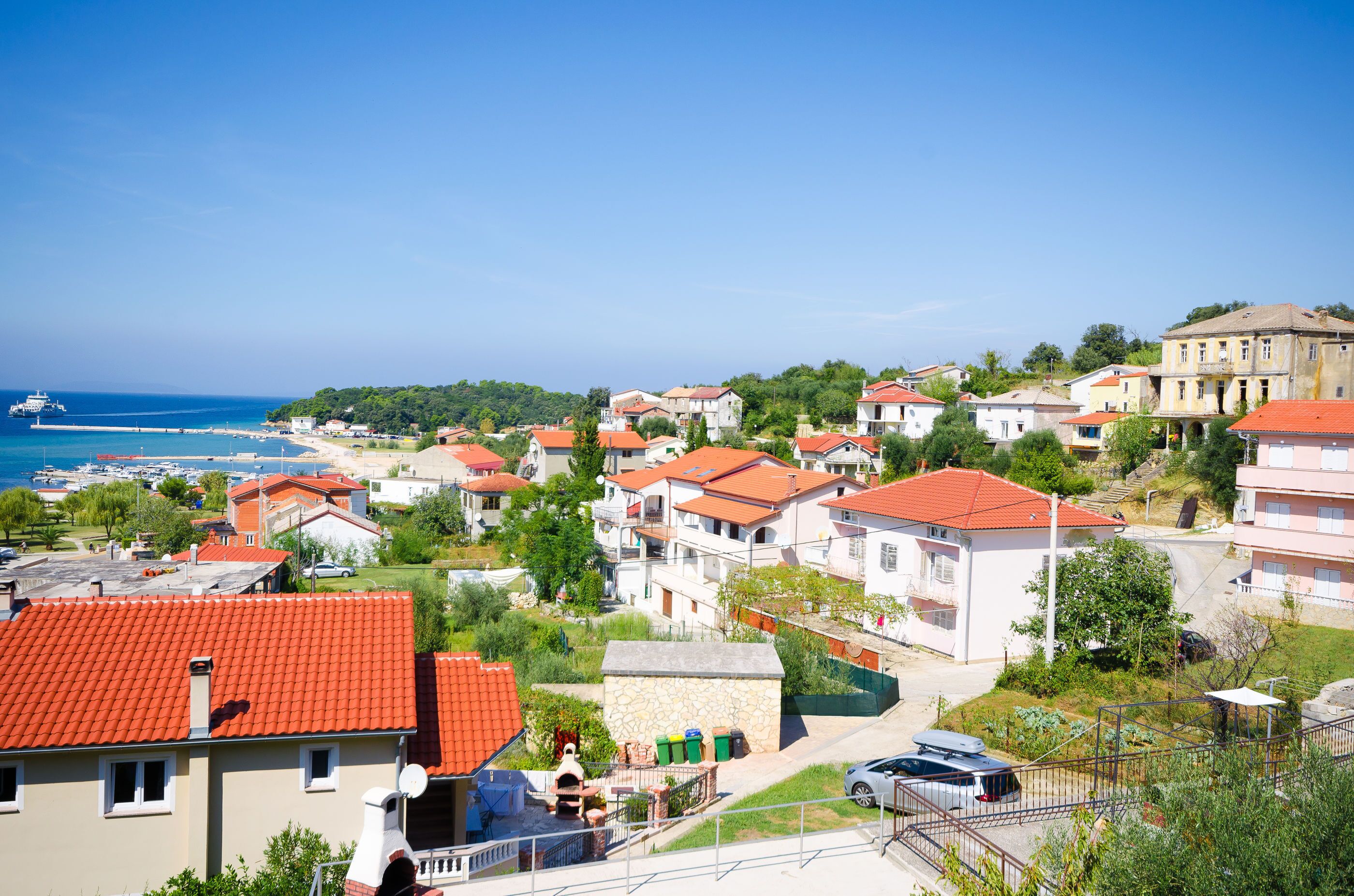 A coastal residential area with red-tiled roofs, a marina, and a mix of single and multi-story buildings.