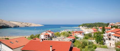 A coastal town with red-roofed buildings, a beach, and a clear blue sea.