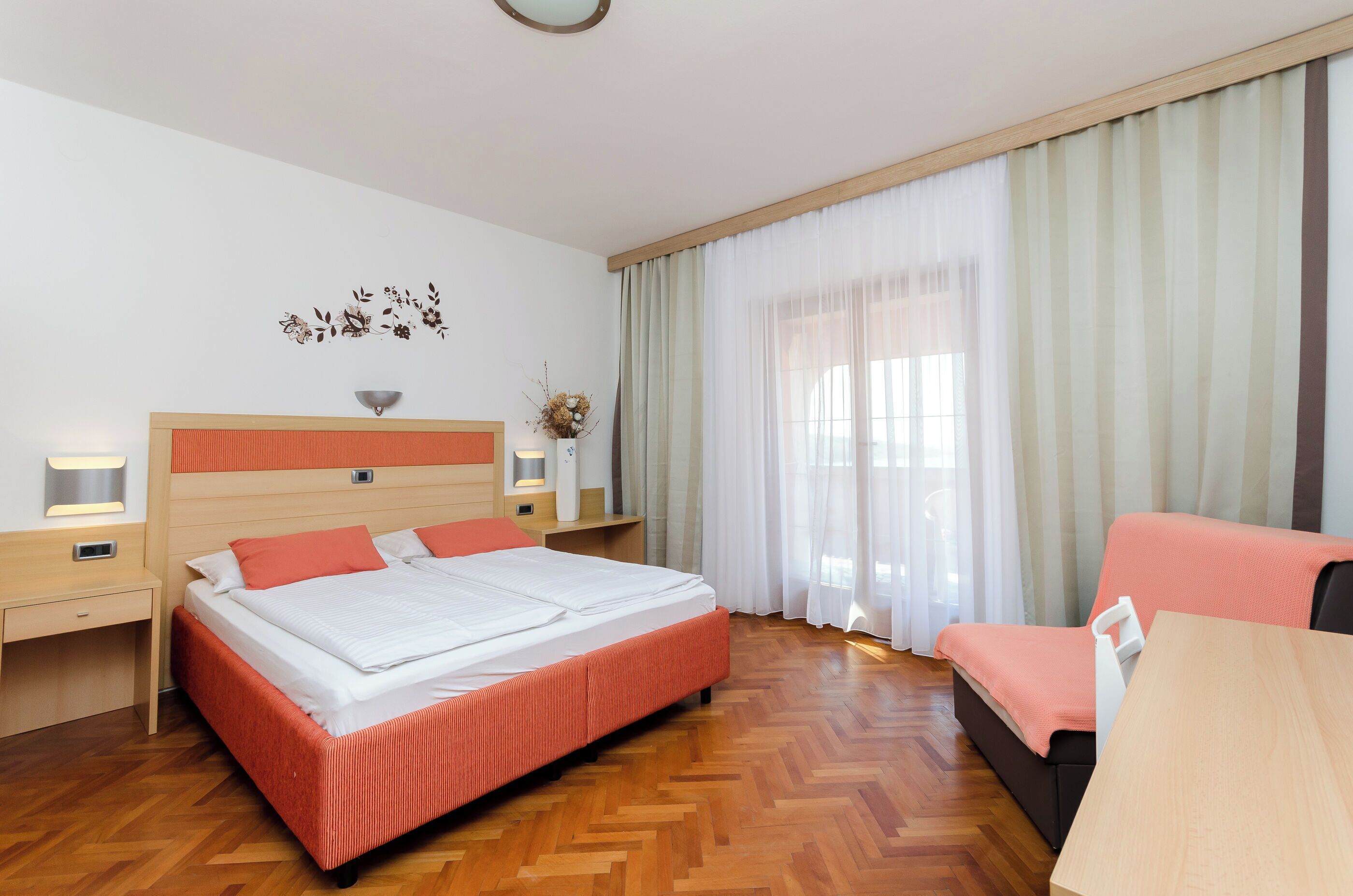 A hotel room with a large bed, a desk, a chair, and a window with curtains.