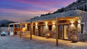 Un edificio de piedra con piscina, pérgolas de madera y grandes jarrones.