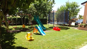 Ein Spielplatz mit Rutschen und Schaukeln, umgeben von Gras und Bäumen.