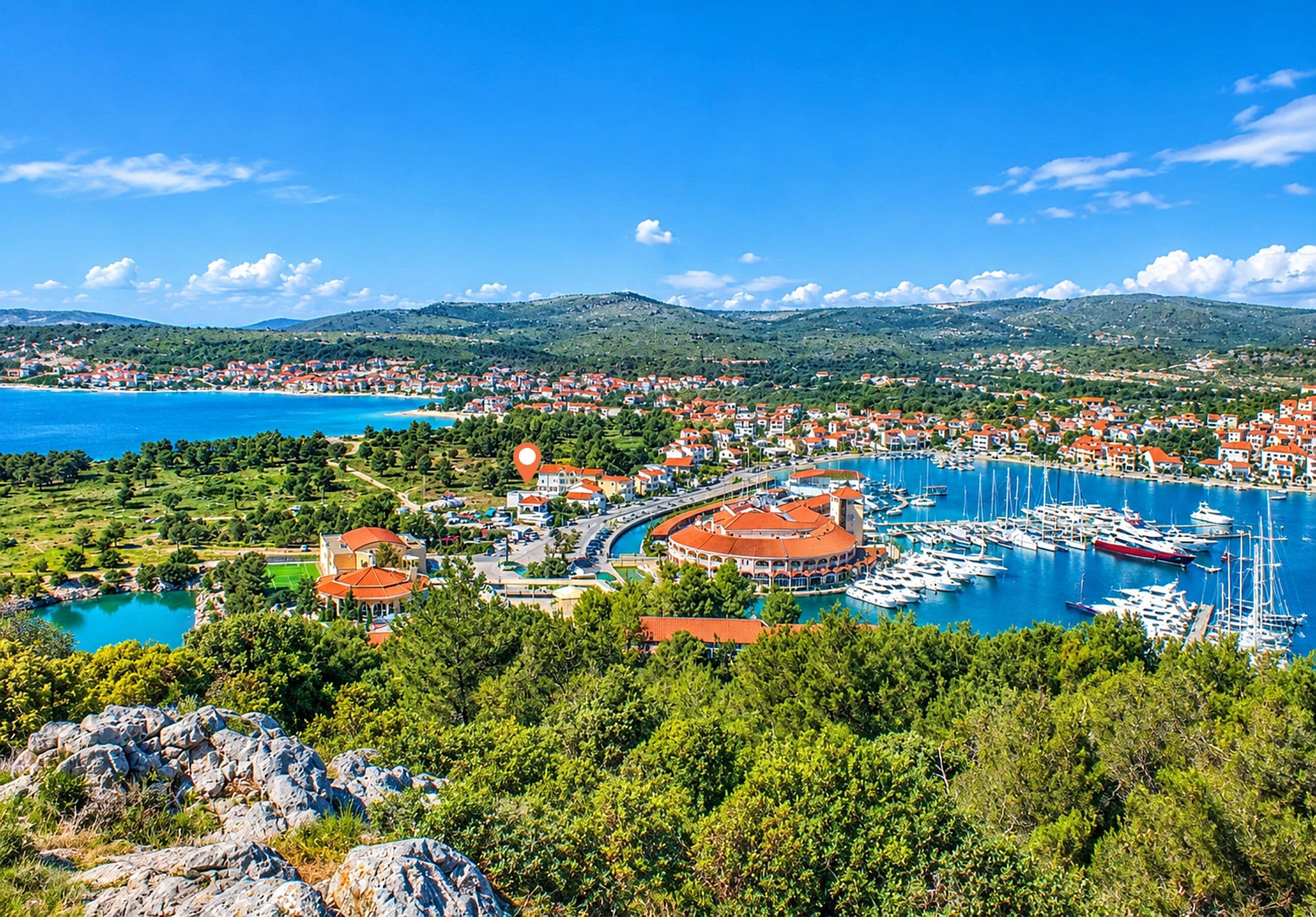 A coastal town with a marina, buildings with red roofs, and a mountainous backdrop.