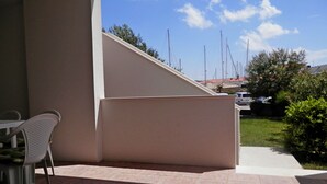 Un espace patio avec une chaise blanche, un sol carrelé et une vue sur des voiliers au loin.
