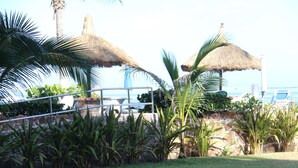 Een tropisch resort met rieten parasols, palmbomen en uitzicht op de oceaan.