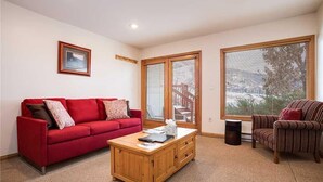 A living room with a red sofa, a wooden coffee table, a striped armchair, and large windows with blinds. - Storm Watch Condominiums - Sw205 (Steamboat Springs)