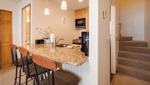 A kitchen with granite countertops, a built-in oven, and a microwave. There are two hanging pendant lights and a clock on the wall. - Storm Watch Condominiums - Sw205 (Steamboat Springs)