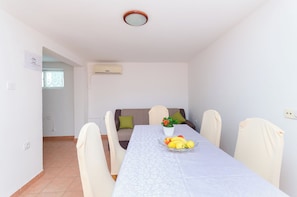 A dining area with a table, chairs, a bowl of fruit, a potted plant, and a sofa. - Apartments Pela (Lopar)