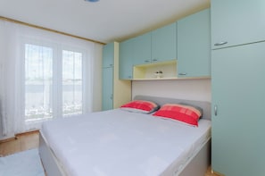 A bedroom with a bed, two pillows, a window with curtains, and light-colored walls. - Apartments Pela (Lopar)