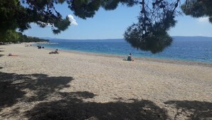 A pebbled beach with people relaxing, clear blue sea, and distant mountains. - House Olive (Tucepi)