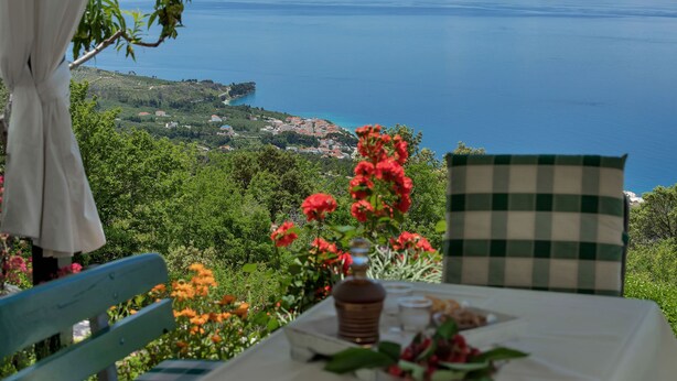 A table with a bottle and glasses, set against a backdrop of a scenic view of a lake and distant hills. - House Olive (Tucepi)