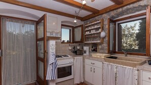 A kitchen with a gas stove, oven, and a sink. There is a window with a view of trees and a stone wall. - House Olive (Tucepi)