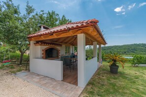 Un espacio de cocina al aire libre techado, con una parrilla, una mesa de comedor y sillas.