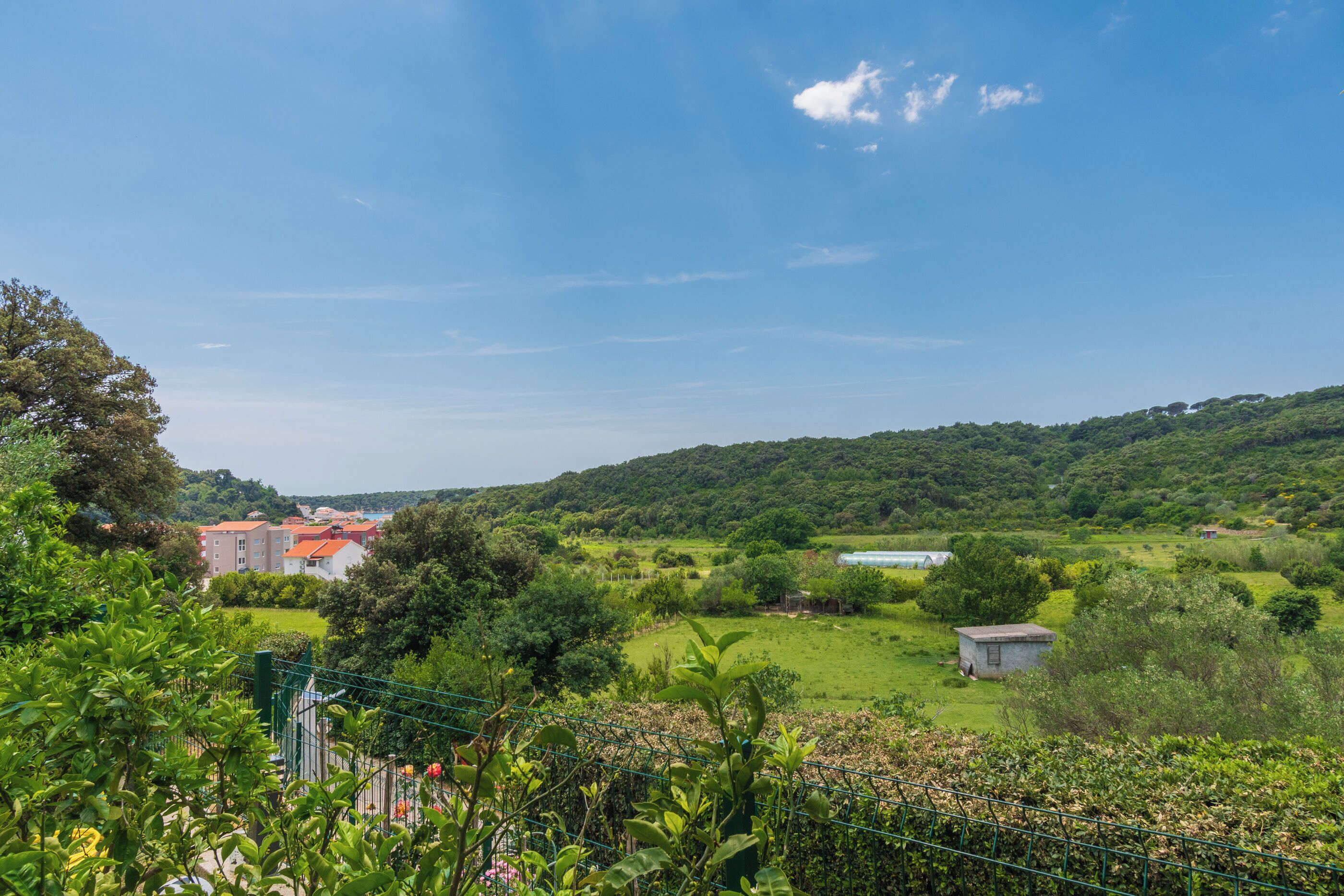 A rural landscape with a small building, a fenced area, and a hill in the background.