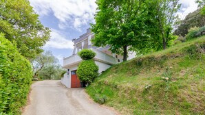 A narrow road leading to a white building with a red door, surrounded by lush greenery and trees. - Apartment Marija (Palit)