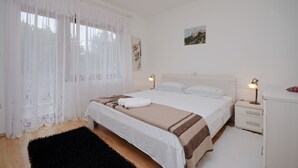 A bedroom with a large bed, a bedside table with a lamp, a nightstand, and a dresser. - Apartment Marija (Palit)