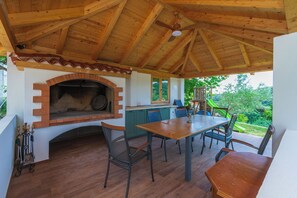 Un patio al aire libre con chimenea de ladrillo, techo de madera y una mesa de comedor con sillas.