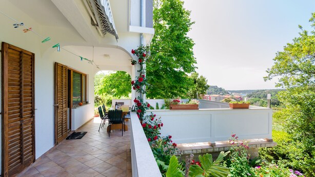 A balcony with a tiled floor, wooden shutters, a table with chairs, and potted plants. - Apartment Marija (Palit)