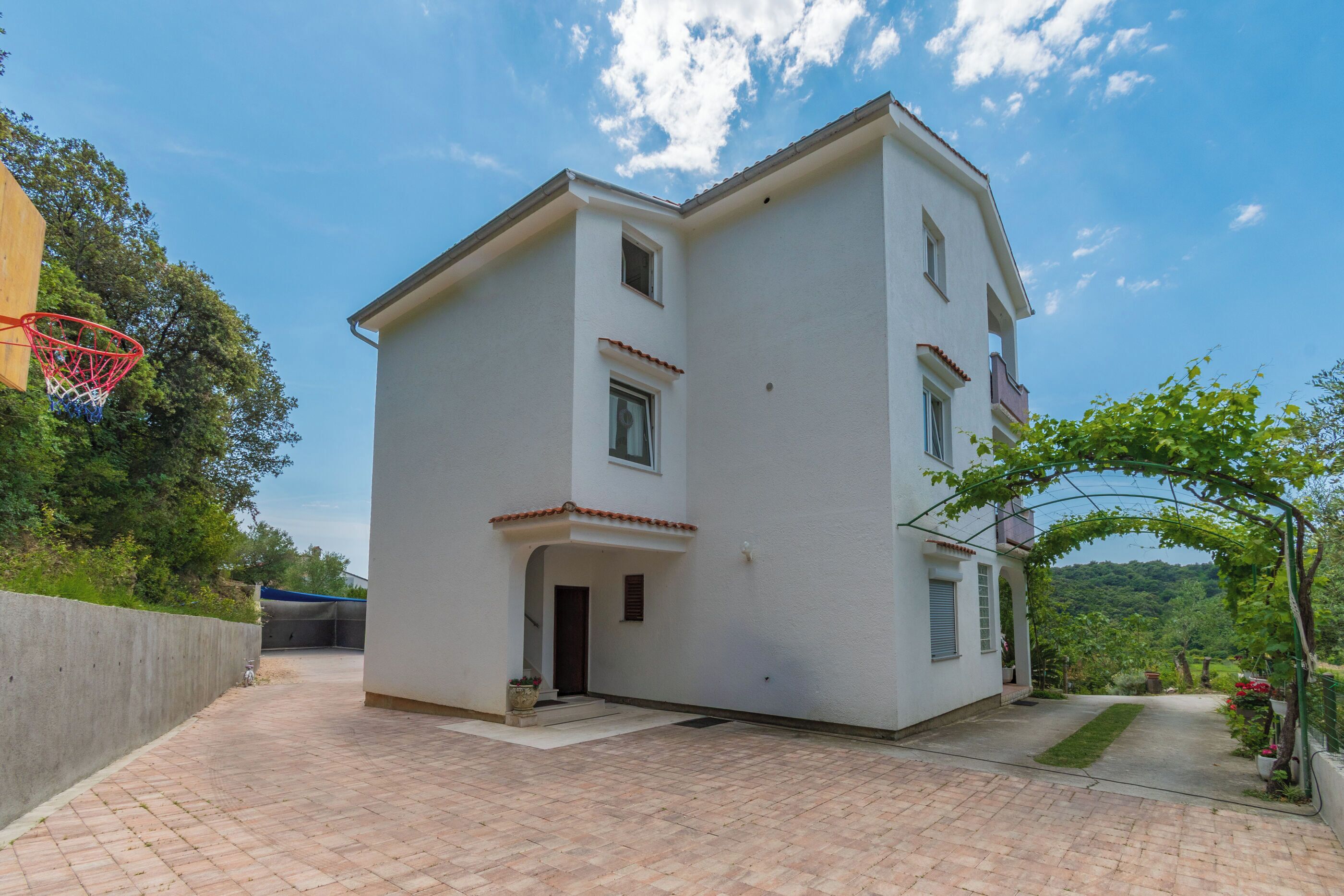 A two-story building with a balcony, a basketball hoop, and a paved driveway.