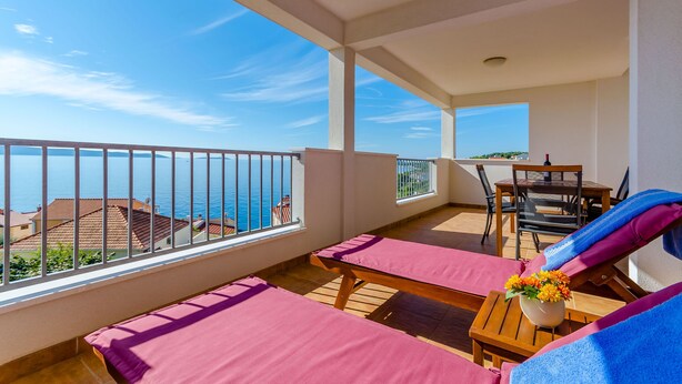 A balcony with two sun loungers, a table with a vase of flowers, and a view of the sea. - Apartments Jurko (Okrug Gornji)
