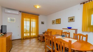 A dining area with a wooden table and chairs, a television on a cabinet, and yellow curtains. - Apartments Jurko (Okrug Gornji)