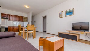 A modern living room with a sofa, a wooden desk, a TV, and a dining area with a table and chairs. - Apartments Jurko (Okrug Gornji)