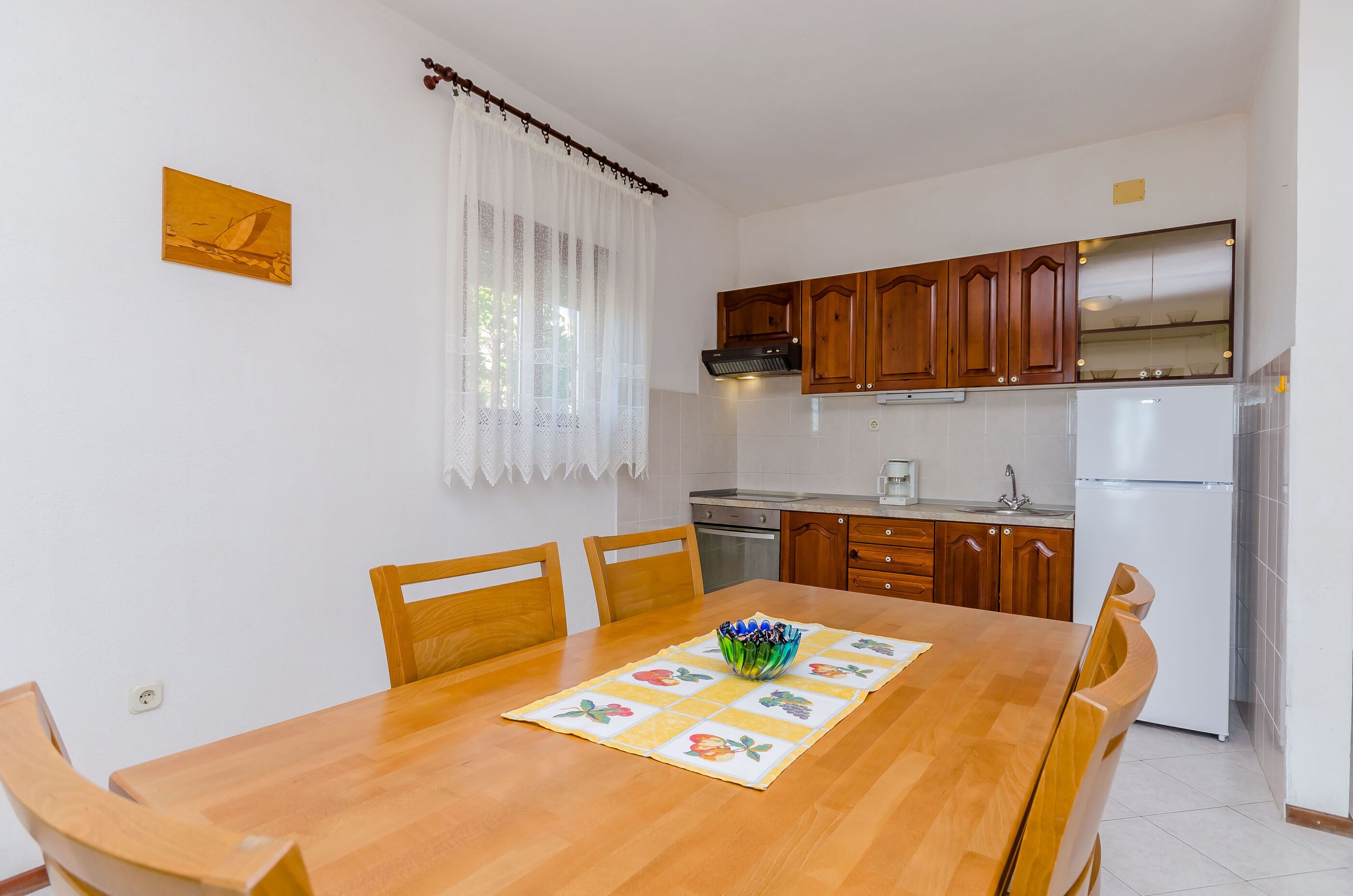 A compact kitchen with wooden cabinets, a white refrigerator, and a dining table with chairs.