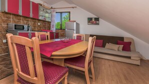 A compact kitchen with red cabinets, a microwave, and a refrigerator. There is a dining table with chairs and a sofa in the living area. - Apartment Ametist (Milna)