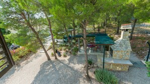 A stone-built outdoor area with a green roof, surrounded by trees and gravel. - Apartment Ametist (Milna)