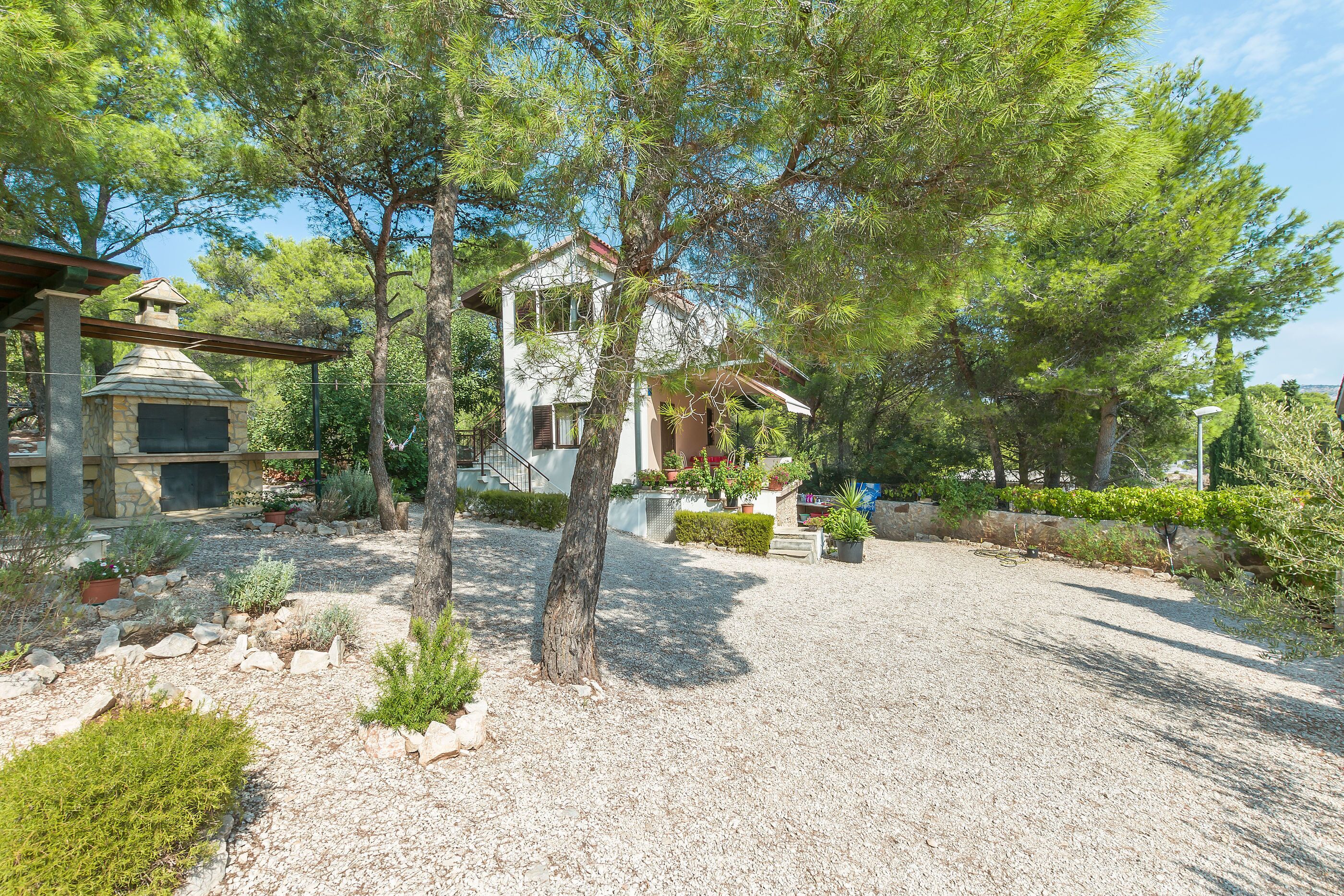 Una casa con chimenea de piedra, rodeada de un camino de grava y diversas plantas.
