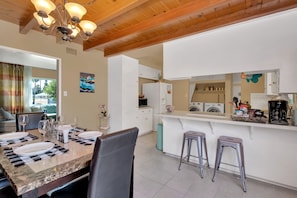 A modern kitchen with white cabinets, a marble countertop, and a built-in oven. There are two bar stools and a dining table set with plates and glasses. - ⭐️offering the Lowest Rate (2000 sqf)-KingBed, Pool Table, 55” Smart TV (Ontario)